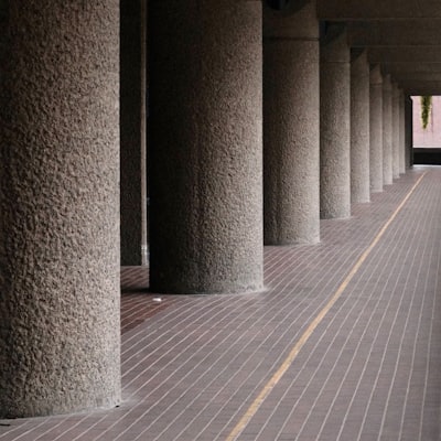 Concrete pillars line a long, dim hallway with brick flooring
